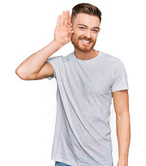 Young redhead man wearing casual grey t shirt smiling with hand over ear listening an hearing to rumor or gossip. deafness concept.