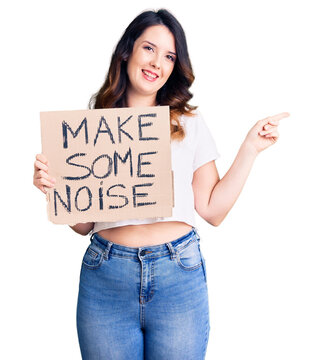 Beautiful young brunette woman holding make some noise banner smiling happy pointing with hand and finger to the side