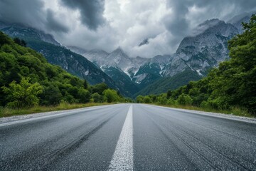 Expansive asphalt road leading towards dramatic mountains under a cloudy sky