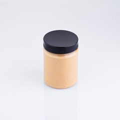 A glass jar filled with a creamy orange sauce has a black lid. It is sitting on a white surface with no other objects in the image.