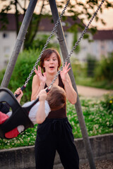 A mother engaging in a playful and animated moment with her young son on a swing at the playground, highlighting joy and togetherness.