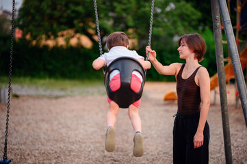 Obraz premium A mother smiling as she spends time with her young son on a swing at the playground, capturing a moment of happiness and bonding outdoors.