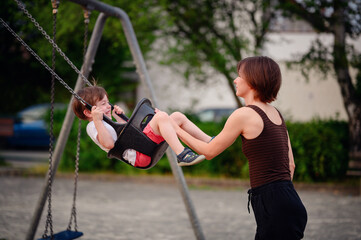 Obraz premium A mother pushing her laughing young son on a swing at the playground, capturing a moment of pure joy and playful bonding together outdoors.