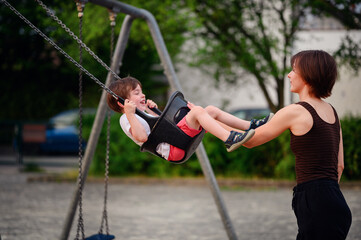 Obraz premium A mother pushing her laughing young son on a swing at the playground, capturing a moment of pure joy and playful bonding together outdoors.