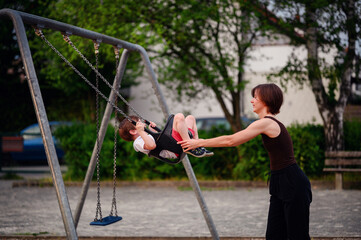 A mother pushing her son on a swing at the playground, both smiling and enjoying a joyful moment of play and bonding outdoors.