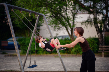 Obraz premium A mother pushing her son on a swing at the playground, both smiling and enjoying a joyful moment of play and bonding outdoors.