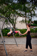 Obraz premium A mother pushing her son on a swing at the playground, both smiling and enjoying a joyful moment of play and bonding outdoors.