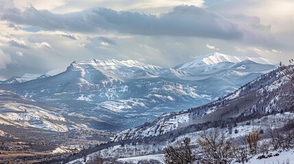 A stunning natural landscape of a snowy mountain range with a cloudy sky creating a dramatic atmosphere. The water in the form of snow covers the mountainous landforms