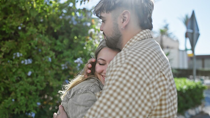 Embracing couple share a tender moment outdoors surrounded by greenery in a serene park.