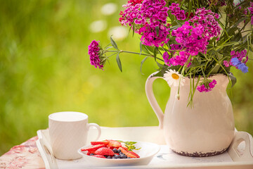 a bouquet of summer flowers and a plate of fruit in the garden on a summer day.