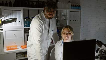 Smiling woman and man in a laboratory with microscope and computer, working as a science team indoors.