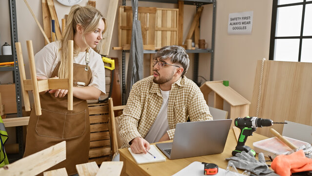 Man and woman working together in a workshop with tools, wood, and a laptop, discussing carpentry design concepts.