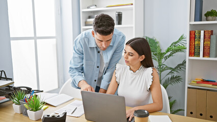 A man and woman collaborate at a laptop in a modern office with plants and books in the background.