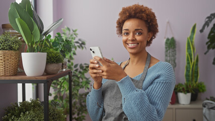 Smiling woman using smartphone amidst lush indoor plants in a cozy home environment, exemplifying...