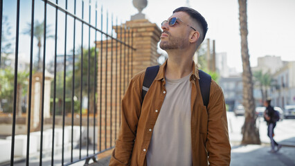 A stylish young hispanic man with a beard strolls casually through an urban cityscape, exuding...