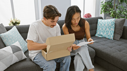 Interracial couple, a man and woman, unpacking together in a cozy, modern living room symbolizing love and a new home.