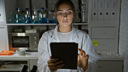 Hispanic woman scientist using tablet in laboratory with glassware background, reflecting healthcare technology integration.