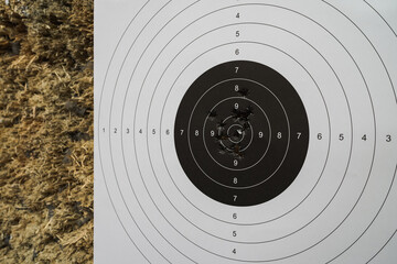 Precision shooting, paper target with bullet holes in the center in a shooting range on a wooden bullet catcher. Close up photo.