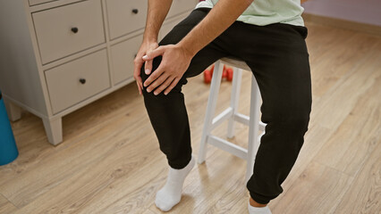 Young man in clinic grasping knee indicating pain, in a healthcare setting.