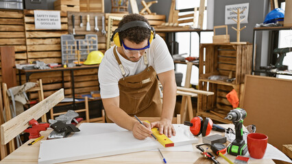 Young man with protective gear measuring wood in a cluttered workshop