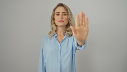 A young blonde woman in a blue shirt gestures stop against a white background.