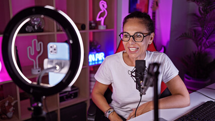 Mature hispanic woman with curly hair streaming in gaming room with neon lights at night.