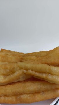Cakwe or Cakue or Youtiao is traditional Chinese snack, long golden-brown deep-fried strip of wheat flour dough and very popular in China and Asia. Close up, rotating in motion.