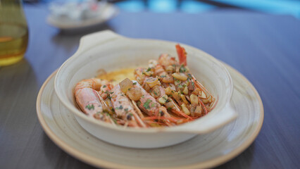 Close-up of delicious garlic shrimp in a white ceramic bowl on a dining table, emphasizing elegant seafood cuisine.