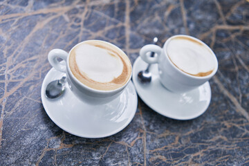 Two cappuccinos with frothy milk in white ceramic cups served on a marbled table, embodying a cozy café ambiance.