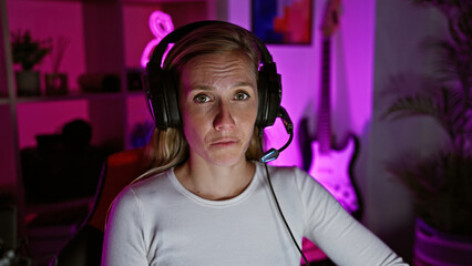 A focused young woman wearing headphones in a dimly lit gaming room at night.