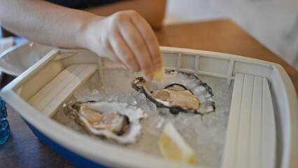 Young beautiful hispanic woman squeezing lemon juice on oysters at the restaurant