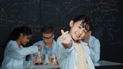 Asian scientist show miniheart to camera while diverse group doing experiment. Young schoolgirl...