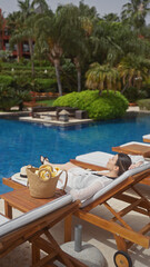 A relaxed woman enjoying the tranquil outdoor setting of a resort poolside in bali, lounging on a deckchair while on vacation.