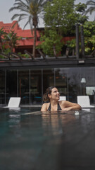 A smiling young woman enjoys tranquility in an outdoor pool at a balinese resort, encapsulating a serene tropical getaway.
