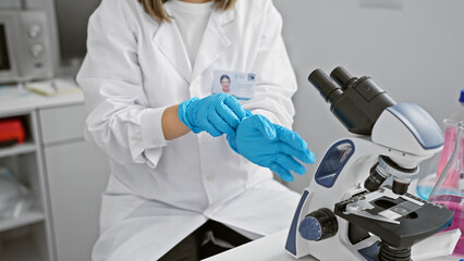 A young woman scientist in a lab wearing a labcoat and blue gloves prepares a microscope for research indoors.