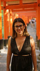 Gorgeous hispanic woman in glasses flaunting a radiant smile at the majestic torii gates of fushimi inari-taisha, kyoto