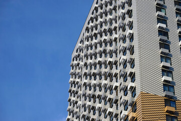 Facade of a modern high-rise residential building with many small balconies against a blue sky.
