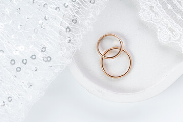 Wedding rings lying on a white concrete tray, white intricate fabric next to it