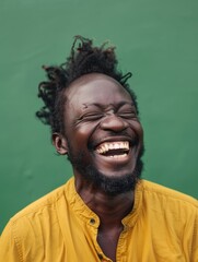Obraz premium A man with dreadlocks is smiling and laughing. He is wearing a yellow shirt. Scene is happy and joyful