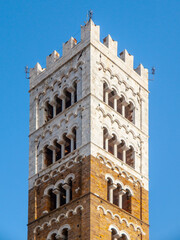 Fototapeta premium The bell tower of Lucca Cathedral, a prominent landmark in Tuscany, Italy, features intricate arches and a blend of brick and stone construction.