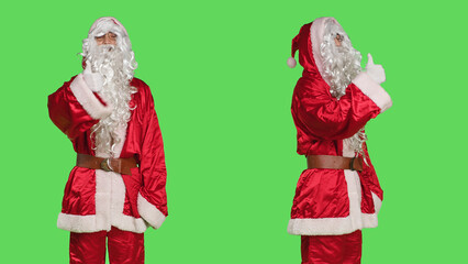 Santa claus doing thumbs up sign wearing costume with hat and white beard, portraying father christmas. Confident man in red suit shows like approval gesture on greenscreen background.