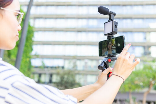 Young woman vlogging outdoors with smartphone and camera