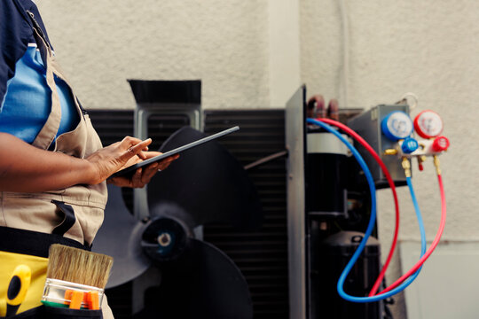 Certified technician commissioned for outside hvac system routine maintenance, looking for refrigerant issues. Competent mechanic doing air conditioner inspection, writing data on tablet