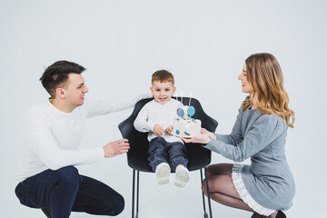 Fototapeta premium A happy married couple with a small son and a delicious cake in their hands. Mom dad and smiling son celebrating birthday. Stylish family.