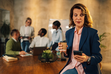 Mature manager typing on phone on meeting of interracial staff at office