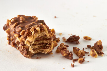 Broken sweet bar made from a wafer covered with caramel and chocolate icing sprinkled with nuts and crumbs on a white background