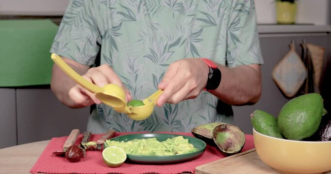 4K video of a man sitting at a table, squeezing lemon on Hass palta with a juicer. Predominantly green, with red, yellow, and gray. Concept of homemade preparation