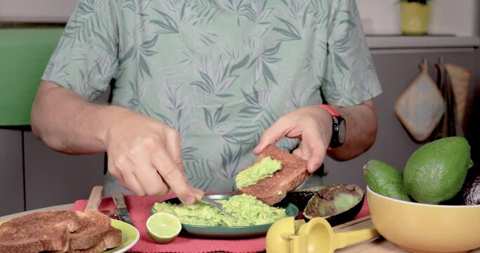 4K video of a man placing Hass palta on toasted bread with a fork. Predominantly green, with red, yellow, and gray. Concept of homemade preparation