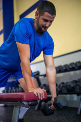 vertical young athlete doing back exercises with dumbbell on gym bench