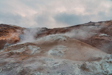 Námafjall Geothermal Area. Tourists in the distance, steaming fumaroles, boiling mud pots. Panorama of suggestive volcanic landscape. Sulfurous springs, solfataras and steam springs.